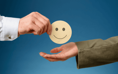Une main donne un smiley souriant en bois à une autre main, symbolisant l'atteinte de la satisfaction client grâce à un service après-vente (SAV) efficace.