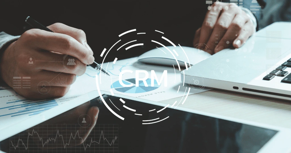 Une personne travaillant sur un ordinateur portable et des documents financiers, avec des graphiques et des icônes numériques superposées, notamment le sigle "CRM", symbolisant l'optimisation de la facturation et la gestion des contrats mensuels - Digitandco.