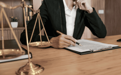 Une personne en costume, près d'une balance de justice, est assise à un bureau et examine un document juridique, symbolisant l'aspect légal des devis et la nécessité de la conformité.