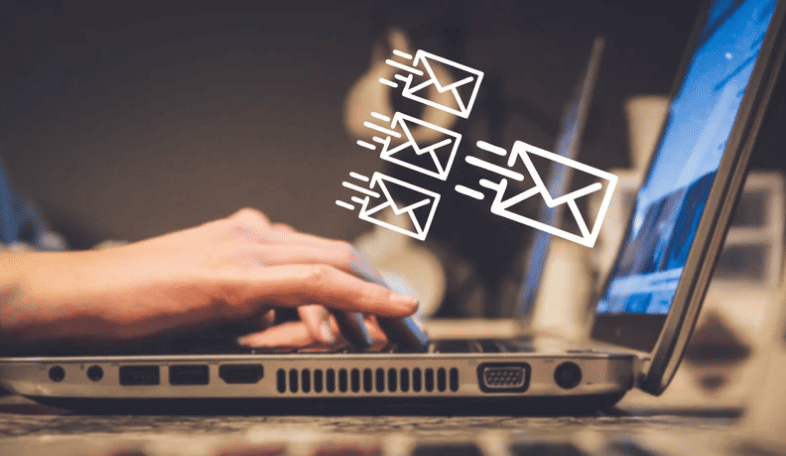 Des mains tapant sur un clavier d'ordinateur portable d'où s'échappent des icônes d'enveloppes en mouvement, symbolisant l'envoi automatisé d'e-mails dans le cadre d'une stratégie de fidélisation client.