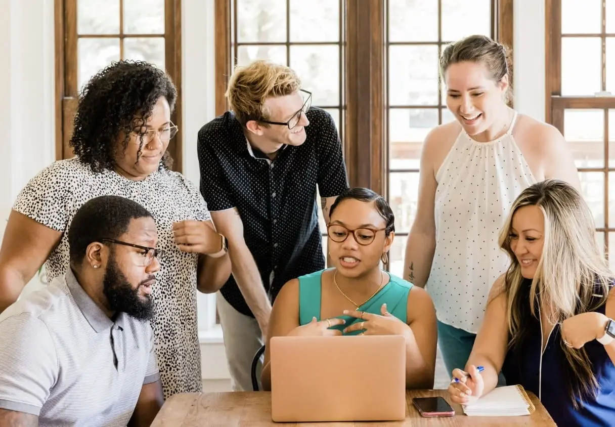 Un groupe de professionnels se réunissant autour d'un ordinateur portable, échangeant et collaborant activement, symbolisant l'importance de la communication et de la coordination d'équipe pour la gestion de projet et l'optimisation d'un planning.