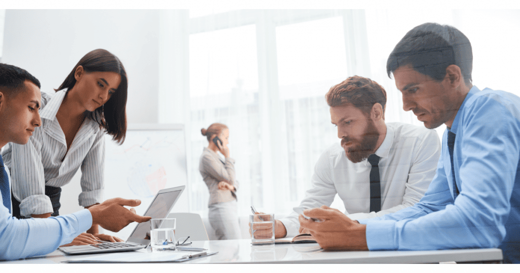 Une équipe de professionnels en réunion de travail, discutant et consultant un ordinateur portable, symbolisant la collaboration et la gestion stratégique d'une communauté en ligne. Une personne au fond est au téléphone. - Digitandco.