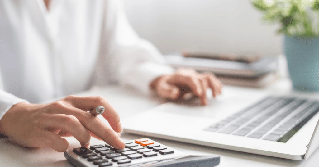 Une personne utilisant une calculatrice avec un stylo à la main, un ordinateur portable en arrière-plan, symbolisant le calcul financier et la préparation de documents importants comme un devis - Digitandco.