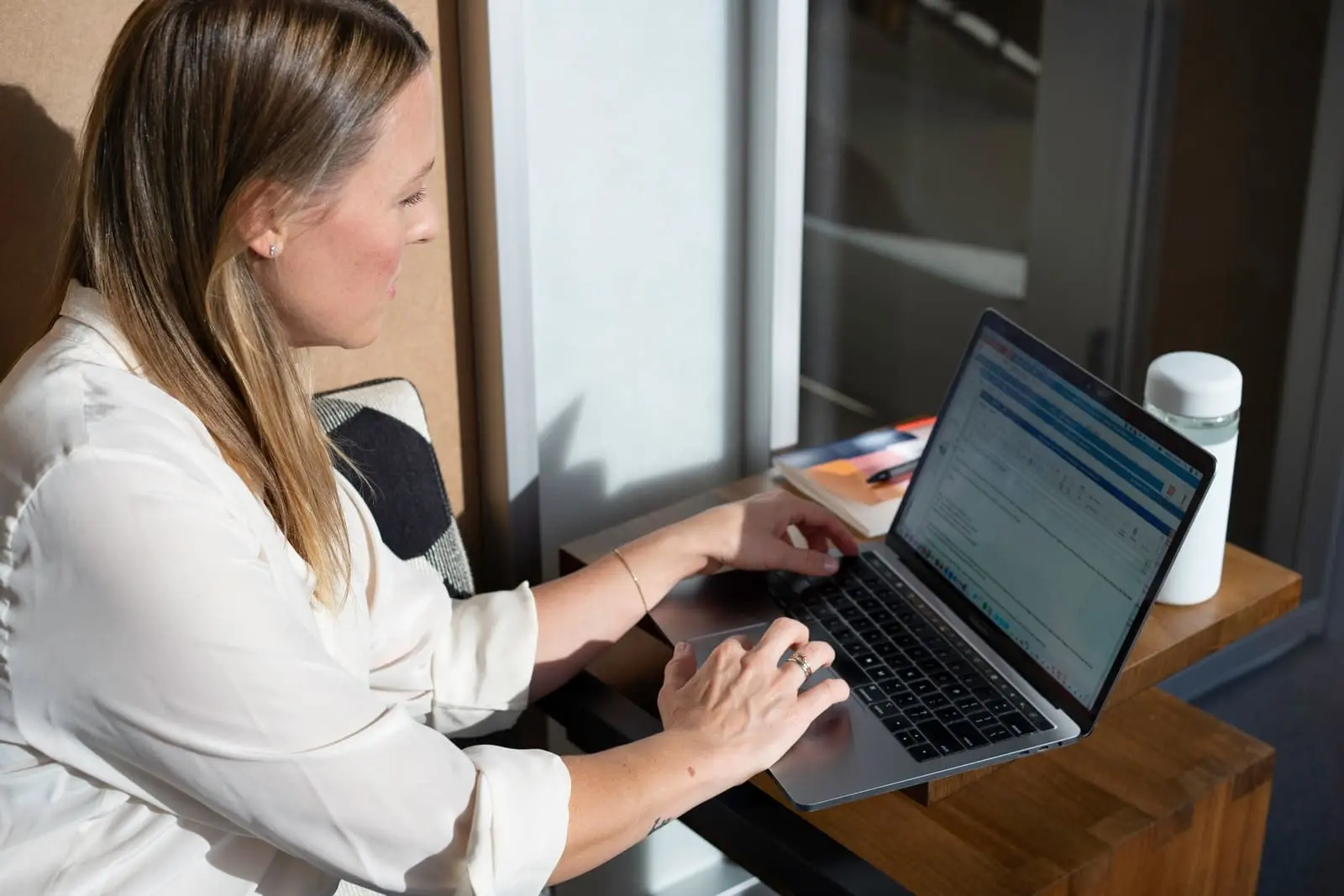 Une femme souriante et concentrée travaillant sur son ordinateur portable, symbolisant la personnalisation stratégique de son profil LinkedIn pour un titre percutant.