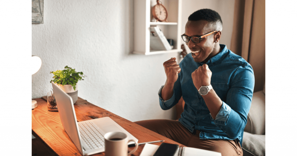 Un homme joyeux et enthousiaste, les poings serrés en signe de victoire, assis devant son ordinateur portable, symbolisant la satisfaction et le succès obtenus grâce au contenu créé pour les réseaux sociaux - Digitandco.