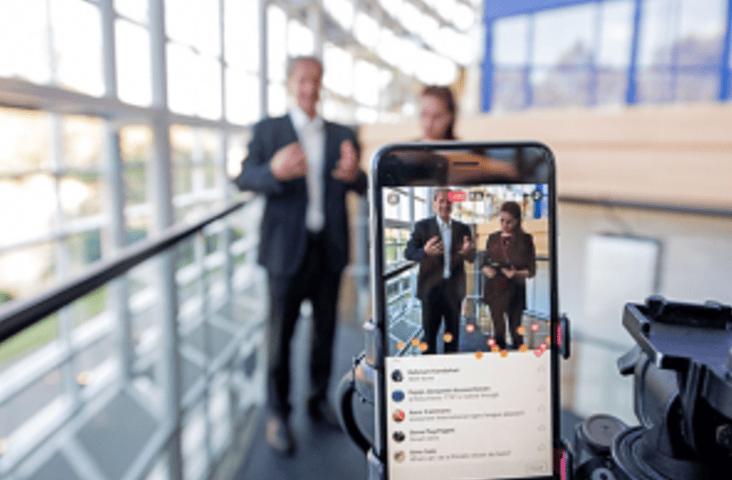 Un smartphone filme en direct deux personnes en tenue de travail, l'écran affichant un live sur les réseaux sociaux. L'image illustre la tendance du live streaming et de la vidéo en direct - Digitandco.