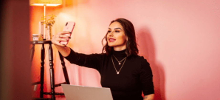 Une jeune femme souriante prend un selfie avec son smartphone, illustrant le rôle des micro-influenceurs dans le marketing digital.