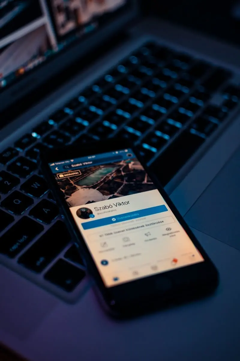 Un smartphone posé sur un clavier d'ordinateur portable, affichant un profil Facebook individuel. L'image est dans une ambiance sombre, mettant en évidence la nature privée du compte personnel.